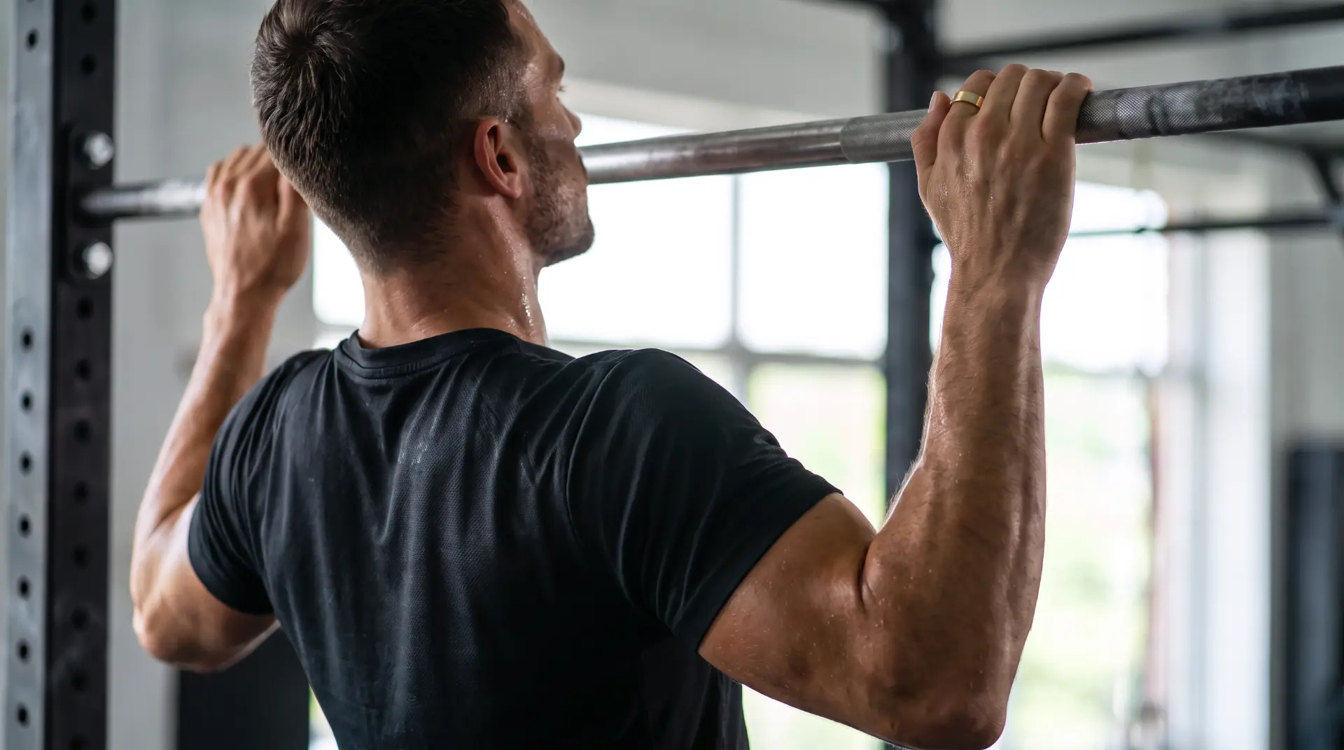 A man doing pull-ups in a gym, wearing a gold ring on his index finger